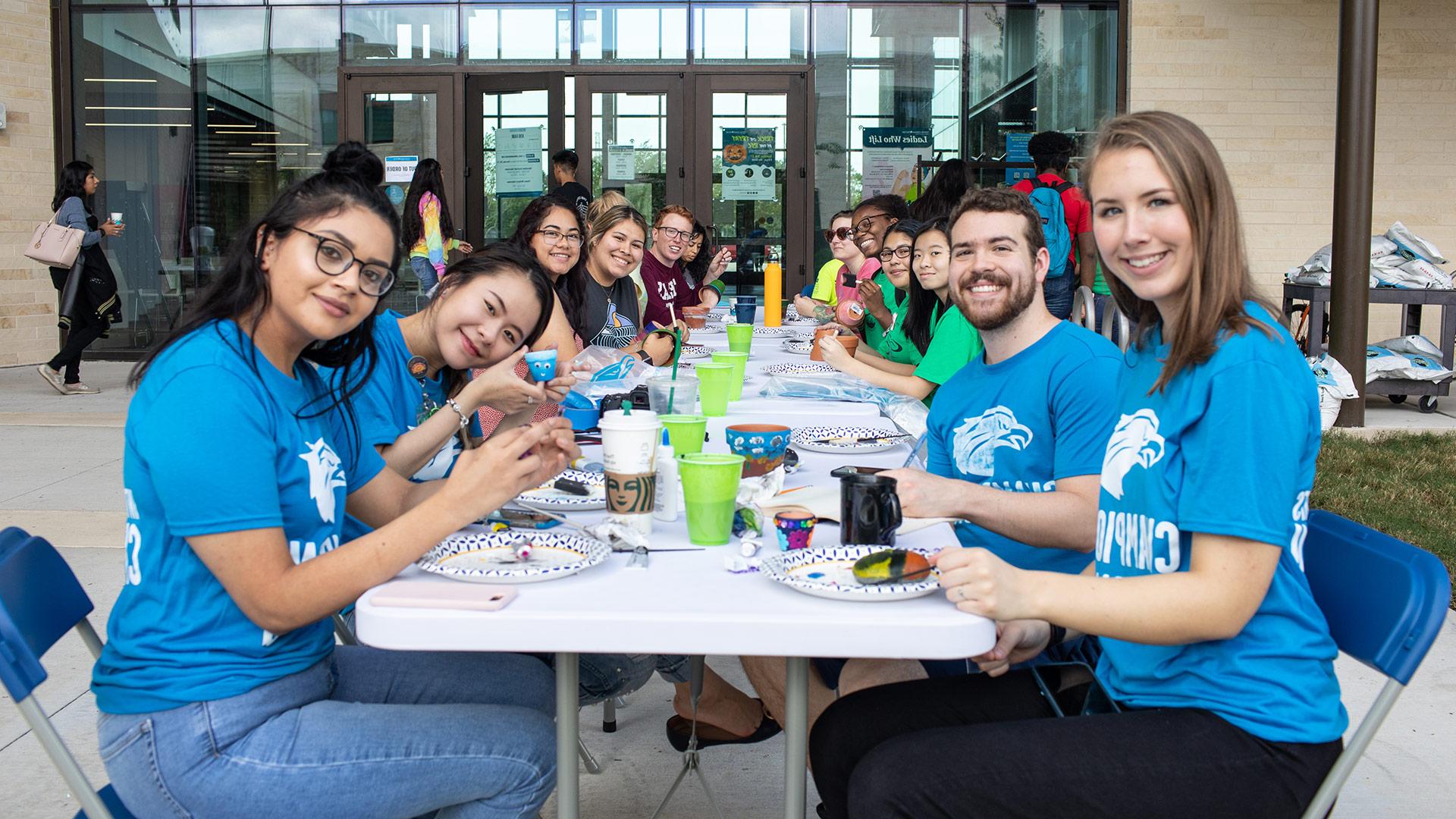穿着蓝色UHCL衬衫的学生聚集在娱乐和健康中心外的学生事务活动桌旁